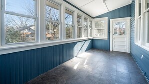 Ein Zimmer mit großen Fenstern, einer Tür und einem Fliesenboden.