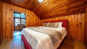 Ein Zimmer mit Holzwänden, einem großen Bett, einem Schreibtisch und einem Fenster.