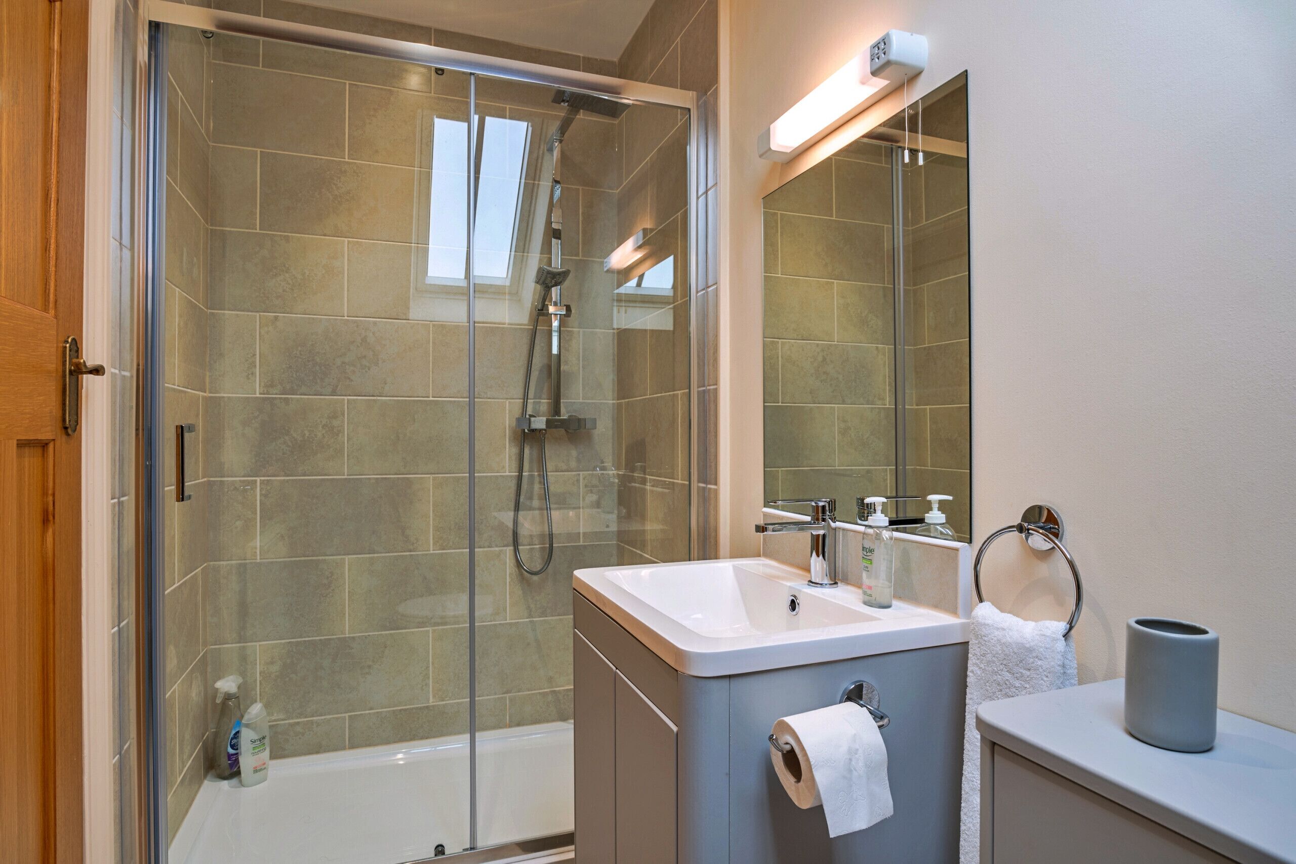 A modern bathroom with a glass-enclosed shower, a sink with a towel ring, and a mirror.