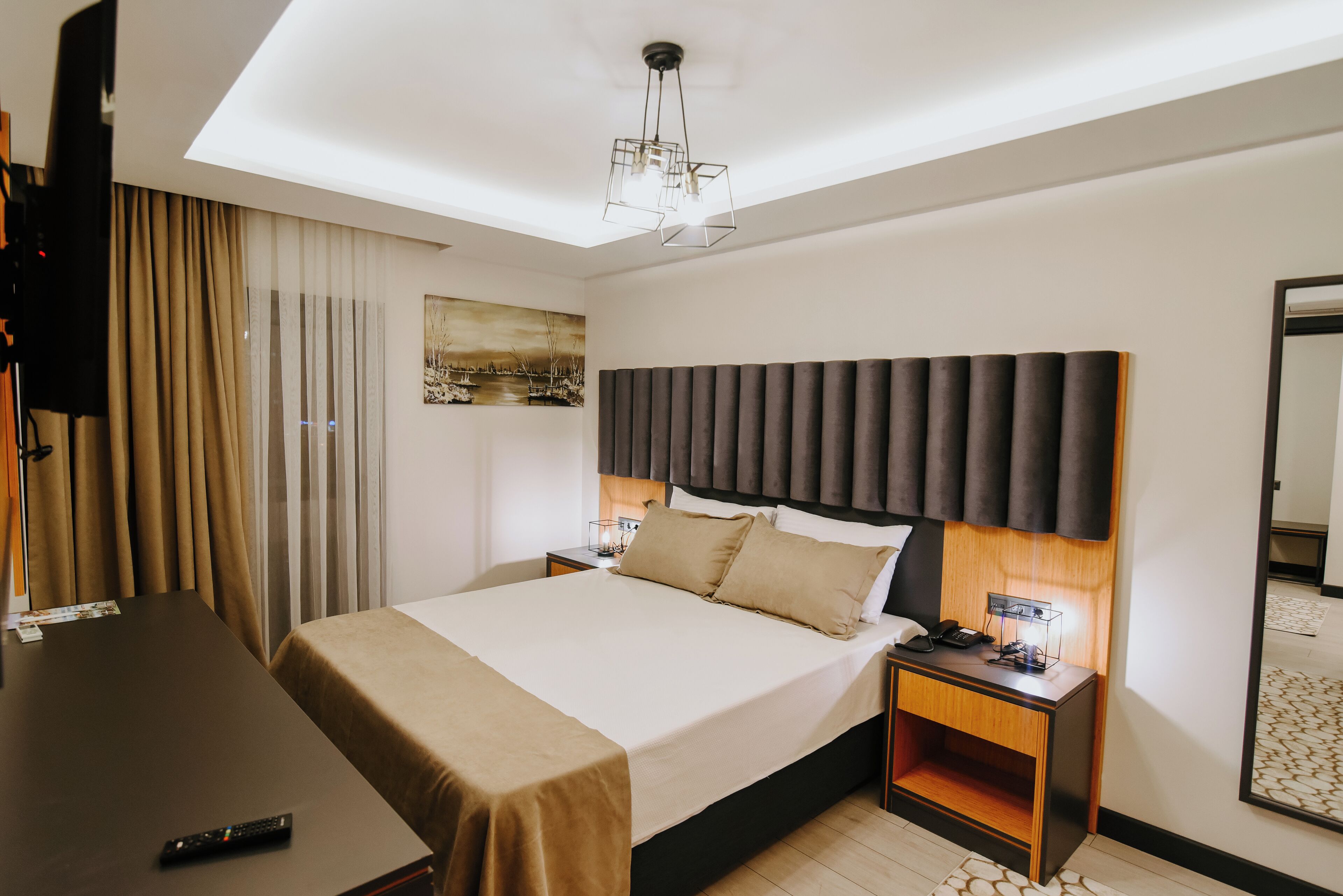A hotel room with a large bed, a desk, a TV, and a ceiling light.