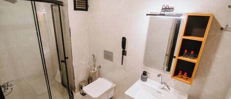 A modern bathroom with a glass shower enclosure, a toilet, a sink with a mirror, and a shelf with toiletries.