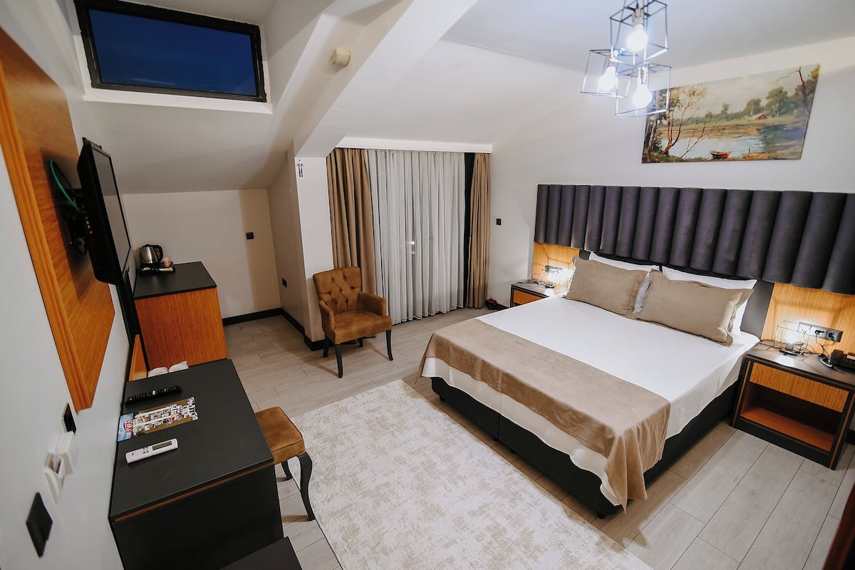 A hotel room with a bed, a desk, a chair, a TV, a painting, and a window.