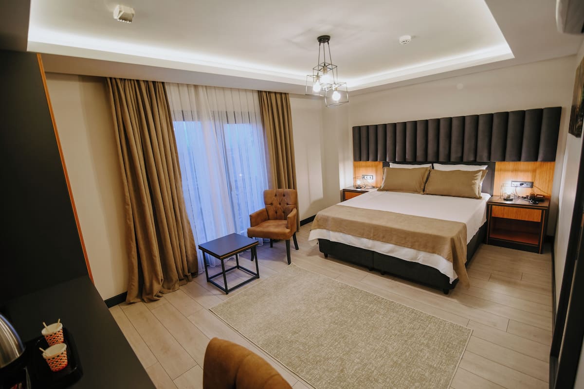 A modern hotel room with a large bed, a chair, a small table, and a desk.