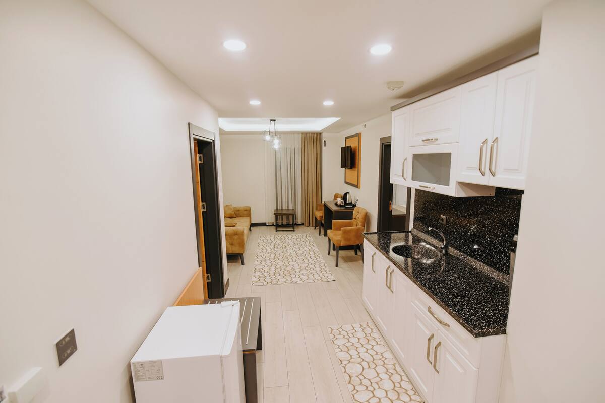 A modern kitchen with white cabinets and a black countertop, a dining area with a table and chairs, and a living room with a sofa and a TV.
