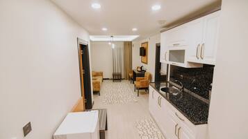 Una cocina moderna con armarios blancos y una encimera negra, una zona de comedor con una mesa y sillas, y una sala de estar con un sofá y televisor.