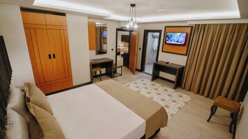 A hotel room with a large bed, a desk, a chair, a television, and a wardrobe.