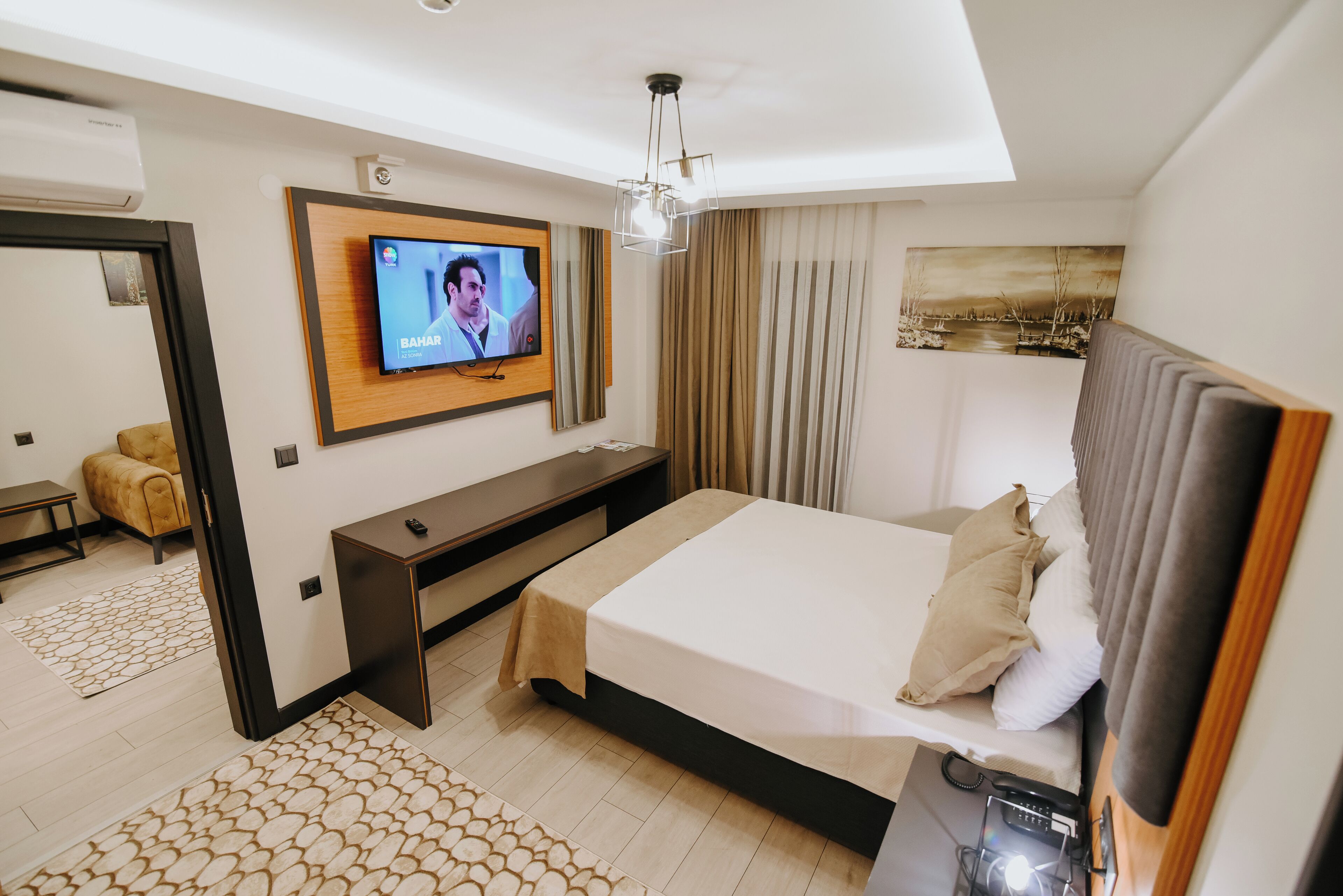 A hotel room with a bed, a TV mounted on the wall, a desk, and a painting.