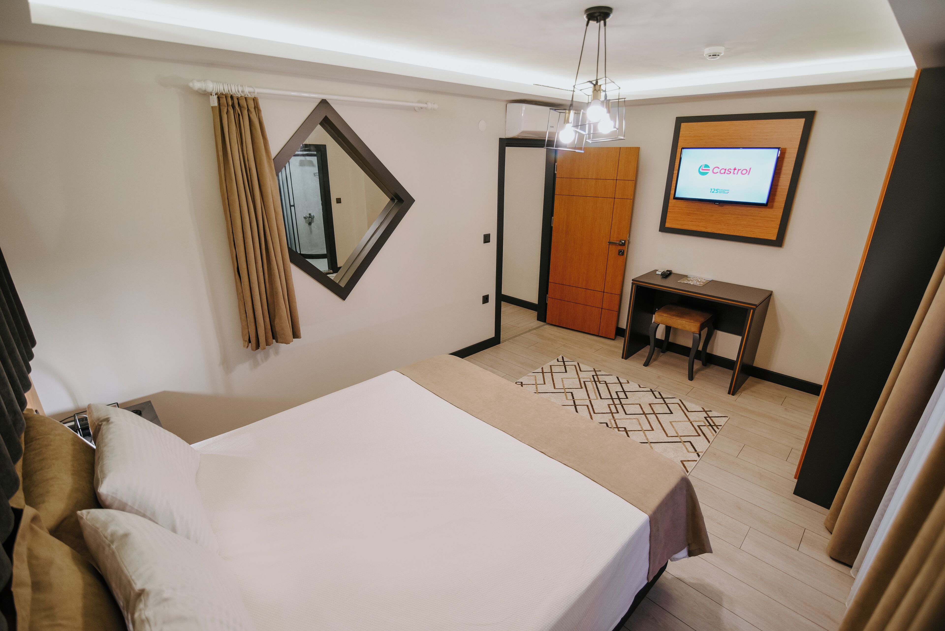 Habitación de hotel con cama, escritorio, armario y televisión mostrando el logotipo de Castrol.