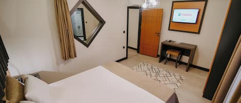Habitación de hotel con cama, escritorio, armario y televisión mostrando el logotipo de Castrol.