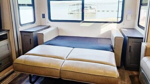 Interior compacto de una caravana con cama, zona de estar y ventana que ofrece vistas al exterior.