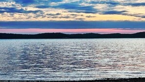 Un lago tranquilo con una orilla lejana, cielo despejado y nubes dispersas.