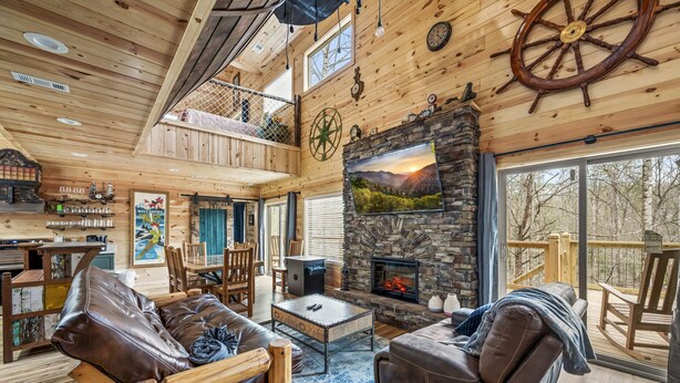 Interior espacioso de una cabaña con chimenea de piedra, muebles de madera y un balcón con vistas al bosque.