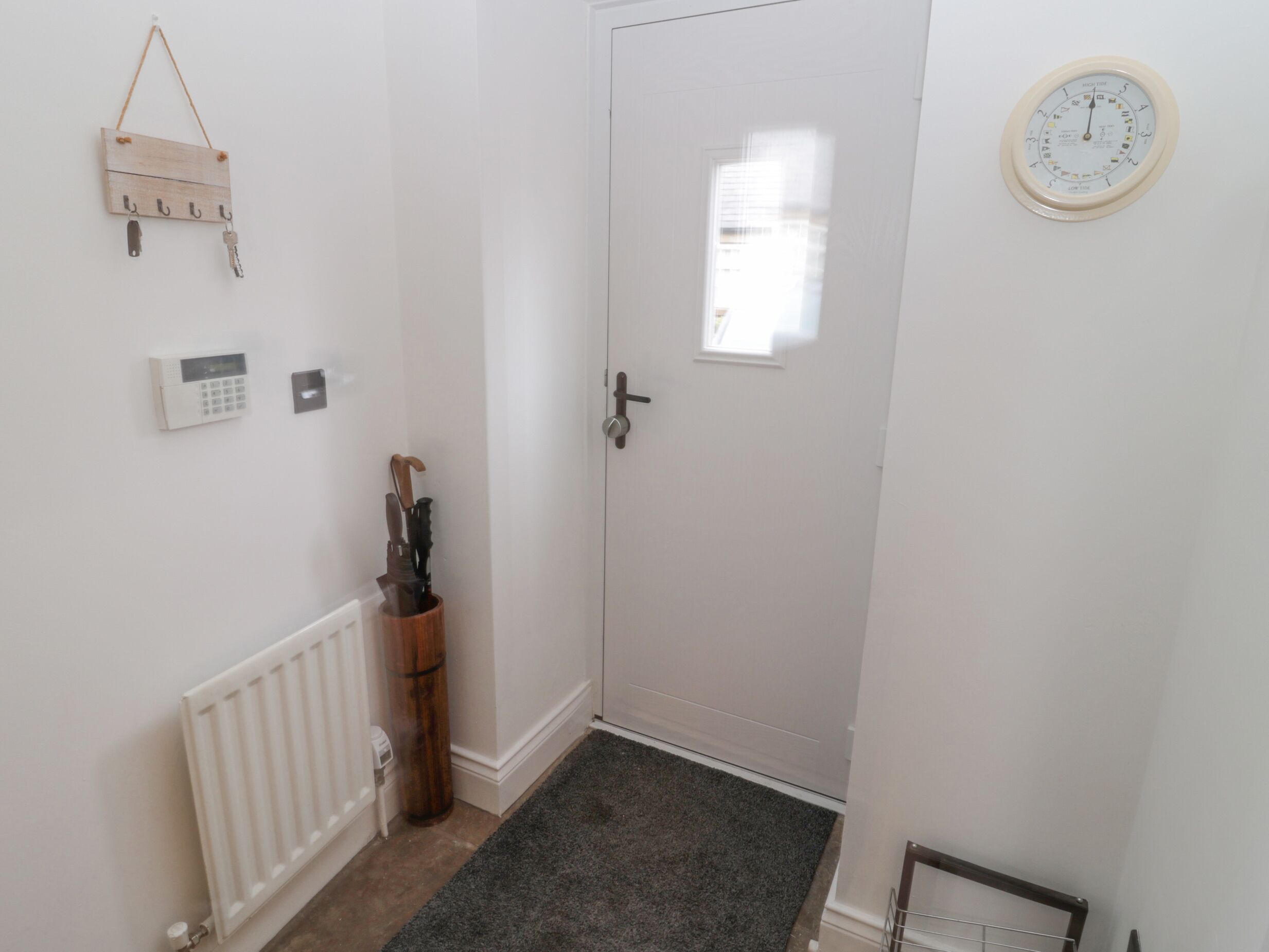A hallway with a white door, a wall-mounted clock, a thermostat, and a wooden coat rack.