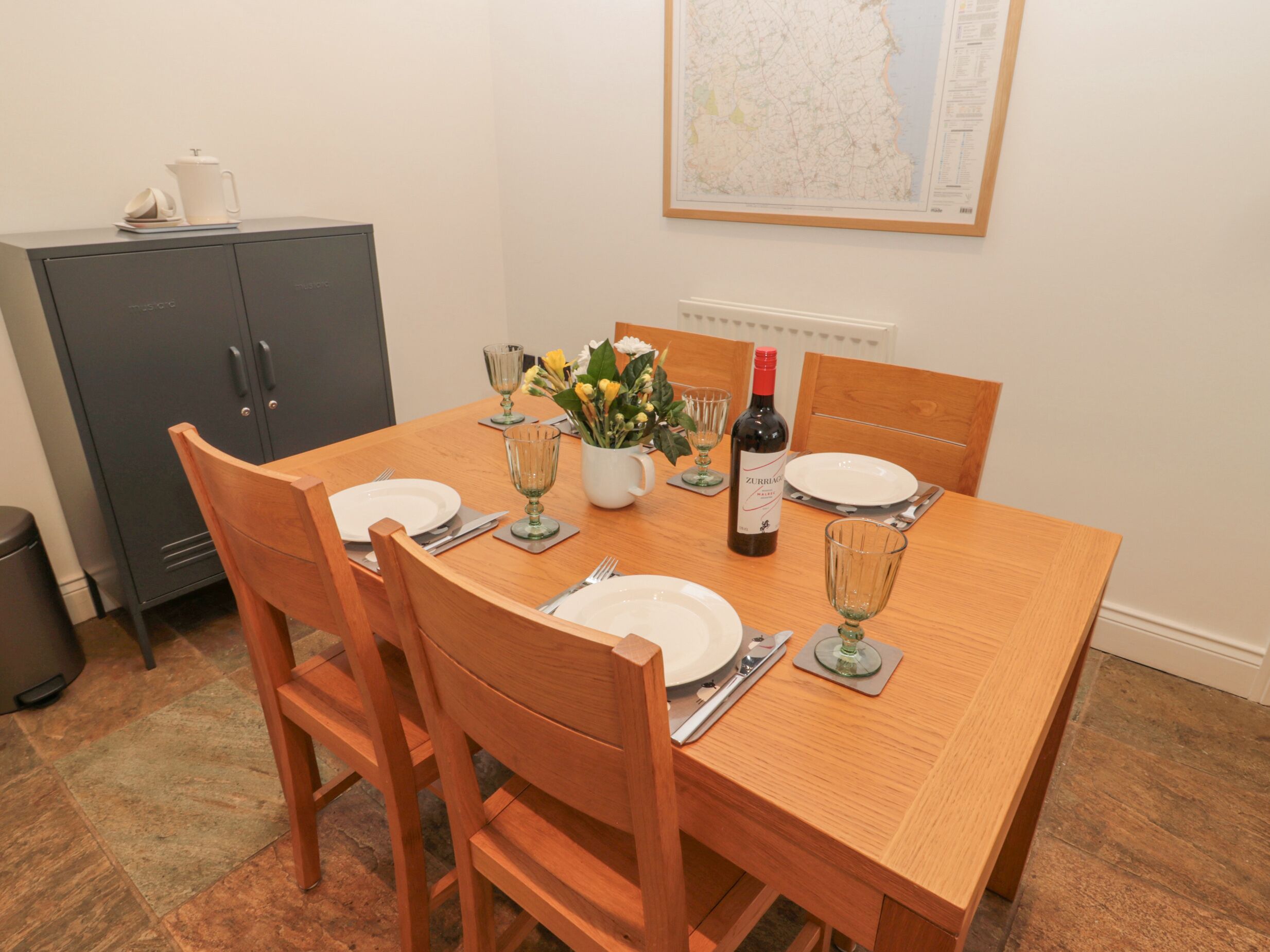 A dining table set with plates, cutlery, wine, and glasses, surrounded by wooden chairs.