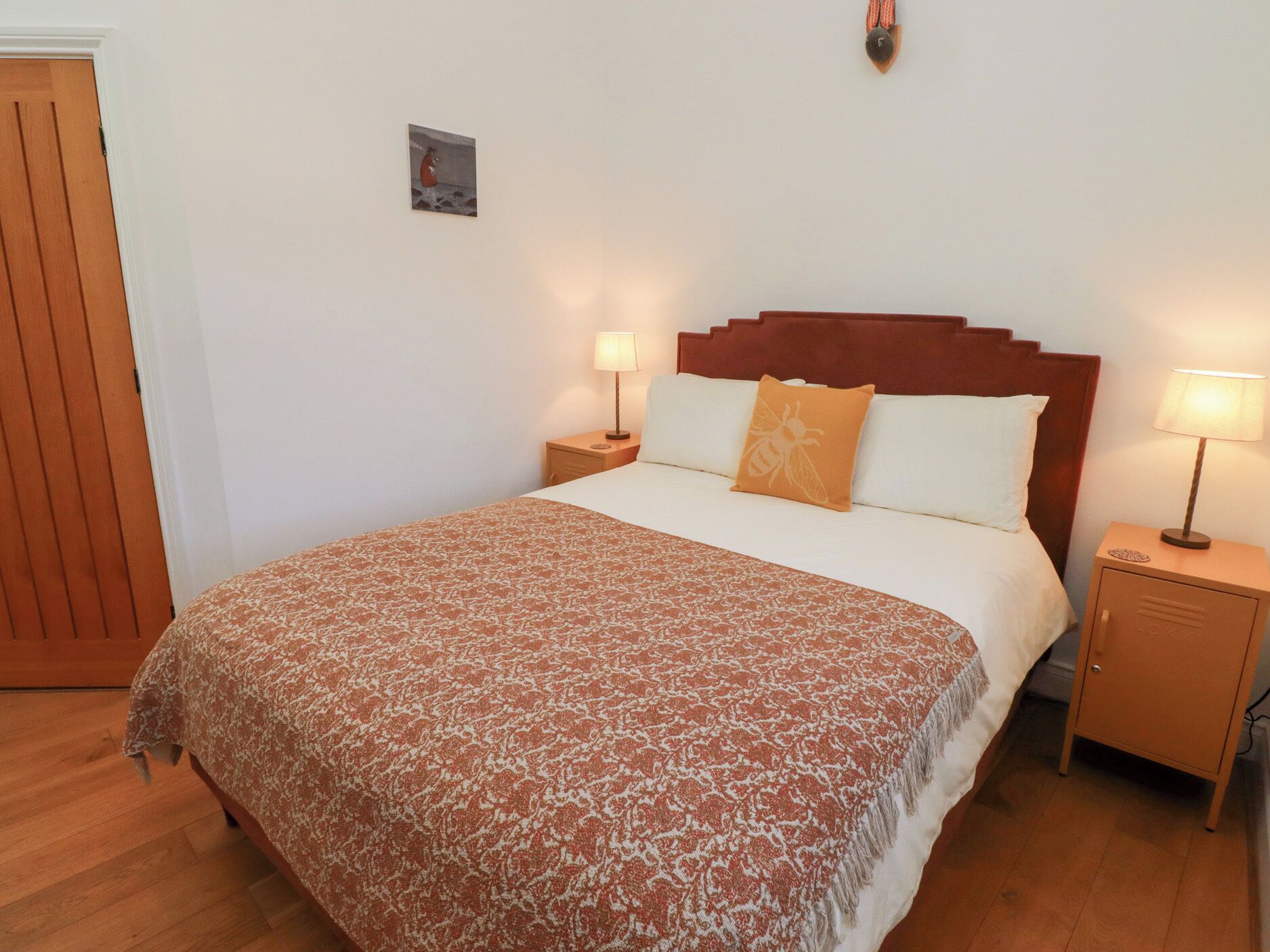 A neatly made bed with a patterned bedspread, two bedside lamps, a wooden headboard, and a small picture on the wall.