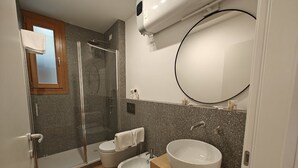 Ett modernt badrum med en dusch som är avskärmad med glasväggar, ett stort handfat och en toalett.