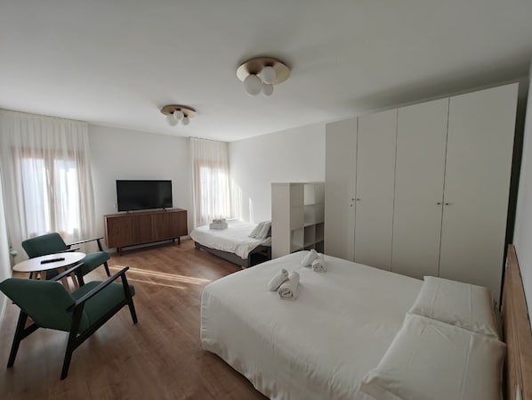 A hotel room with a bed, a desk, a chair, a TV, and a wardrobe.