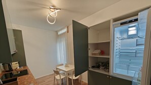 Ett kompakt kök med ett inbyggt kylskåp, ett matbord med stolar och en diskho.