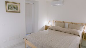 A bedroom with a bed, bedside tables, a wall-mounted air conditioner, and a door.