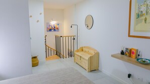Un interior moderno con un banco de madera, un estante pequeño con objetos decorativos y un cuadro en la pared.