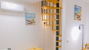 Una habitación moderna con una escalera de madera, un cofre de madera, una mesita con una tetera y un cuadro en la pared.