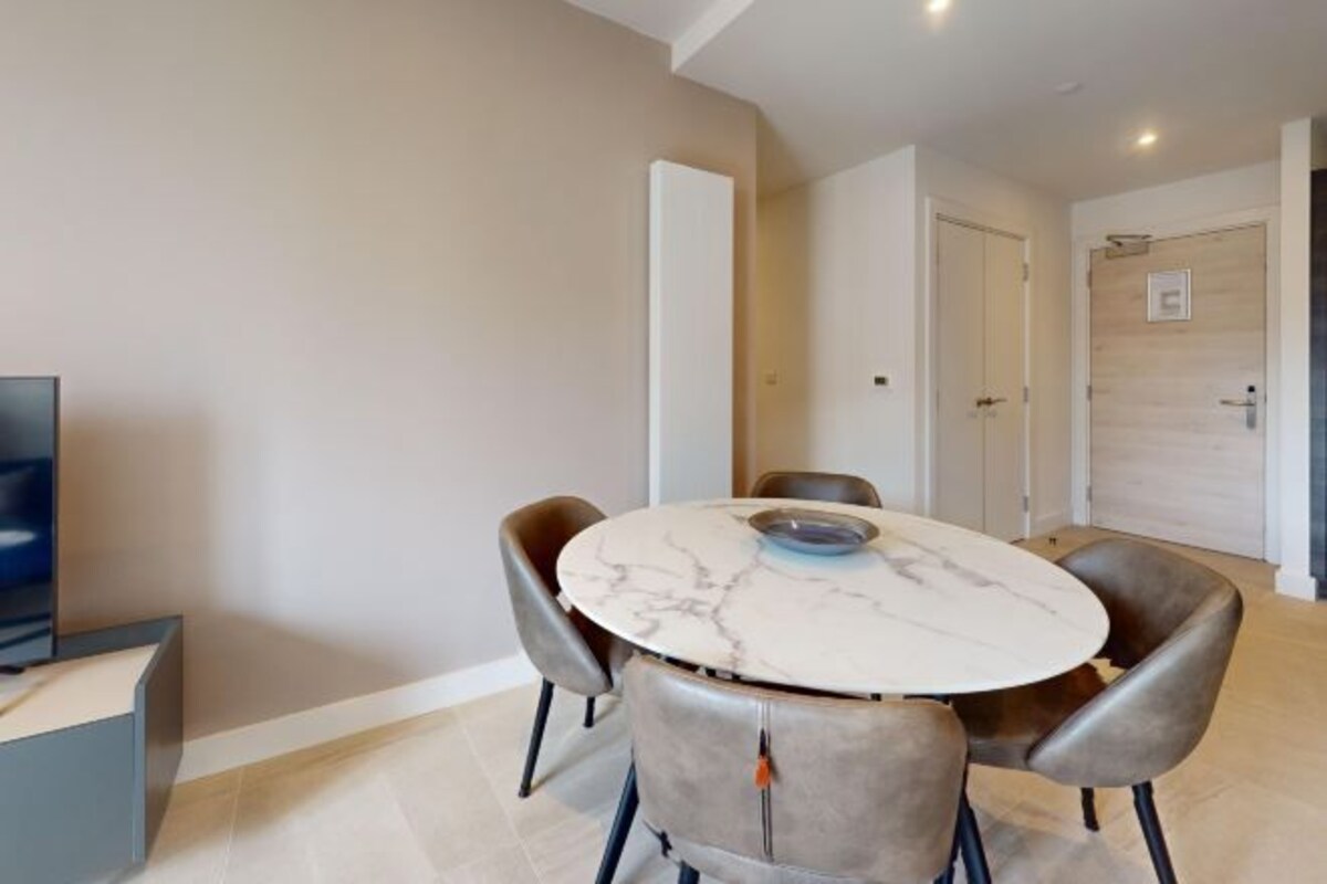 A modern dining area with a marble table and leather chairs, a television, and a door leading to another room.