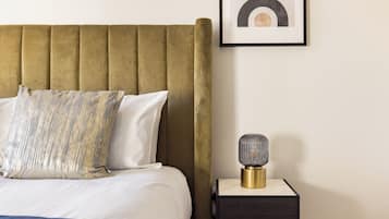 Una cama bien hecha con un cabecero dorado, una almohada estampada y una mesita de noche con una lámpara.