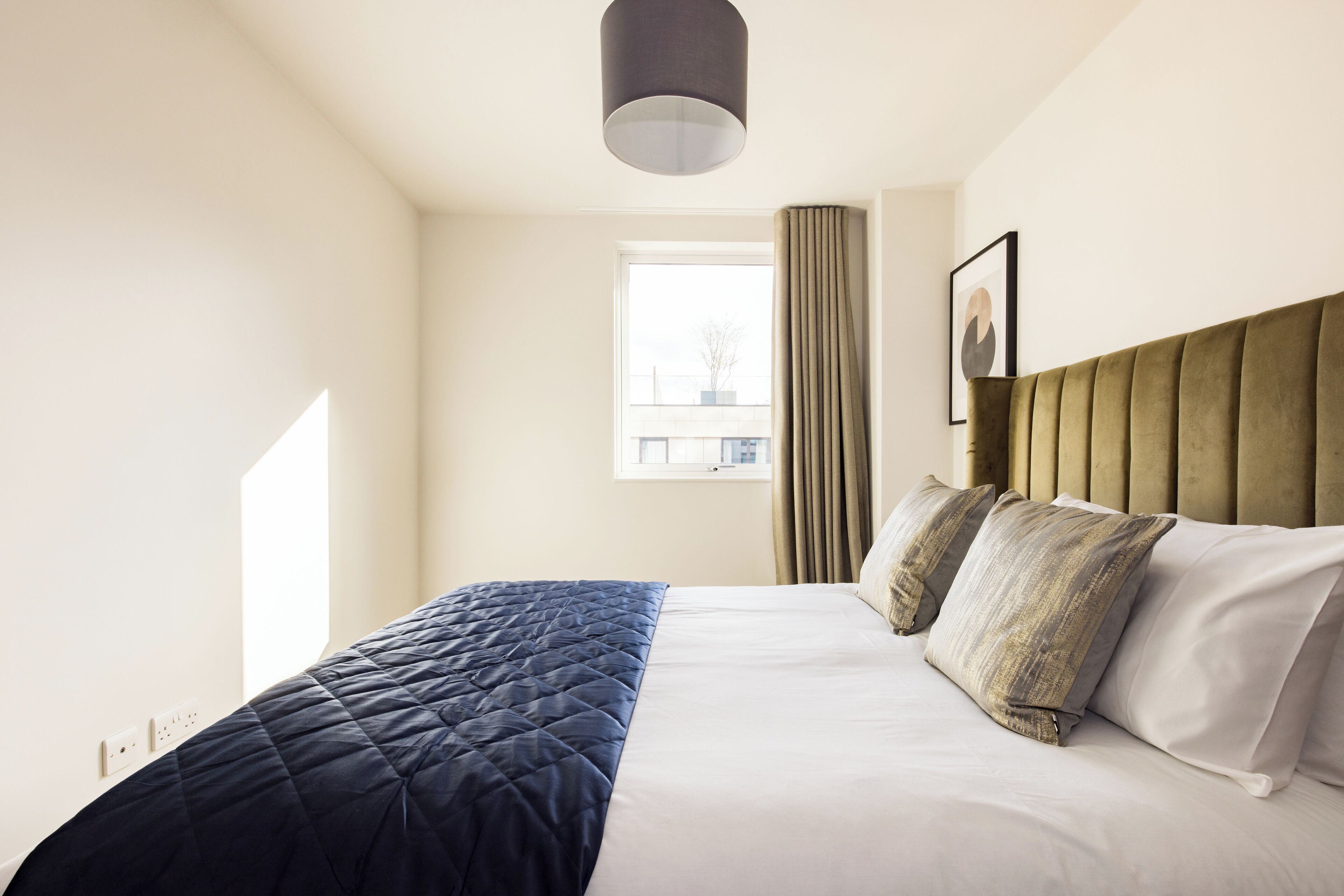 A neatly made bed with a quilted cover, a headboard, and a framed picture on the wall.