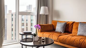 Een moderne woonkamer met een bank, een salontafel, een lamp en uitzicht op de stad door grote ramen.