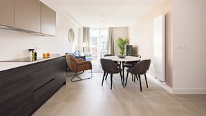 Une cuisine moderne avec des meubles de couleur sombre, un îlot central et un coin repas comprenant une table ronde et des chaises.