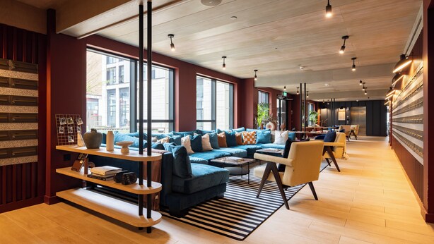 Un salon moderne avec un canapé d’angle bleu, des étagères en bois et un tapis à rayures.
