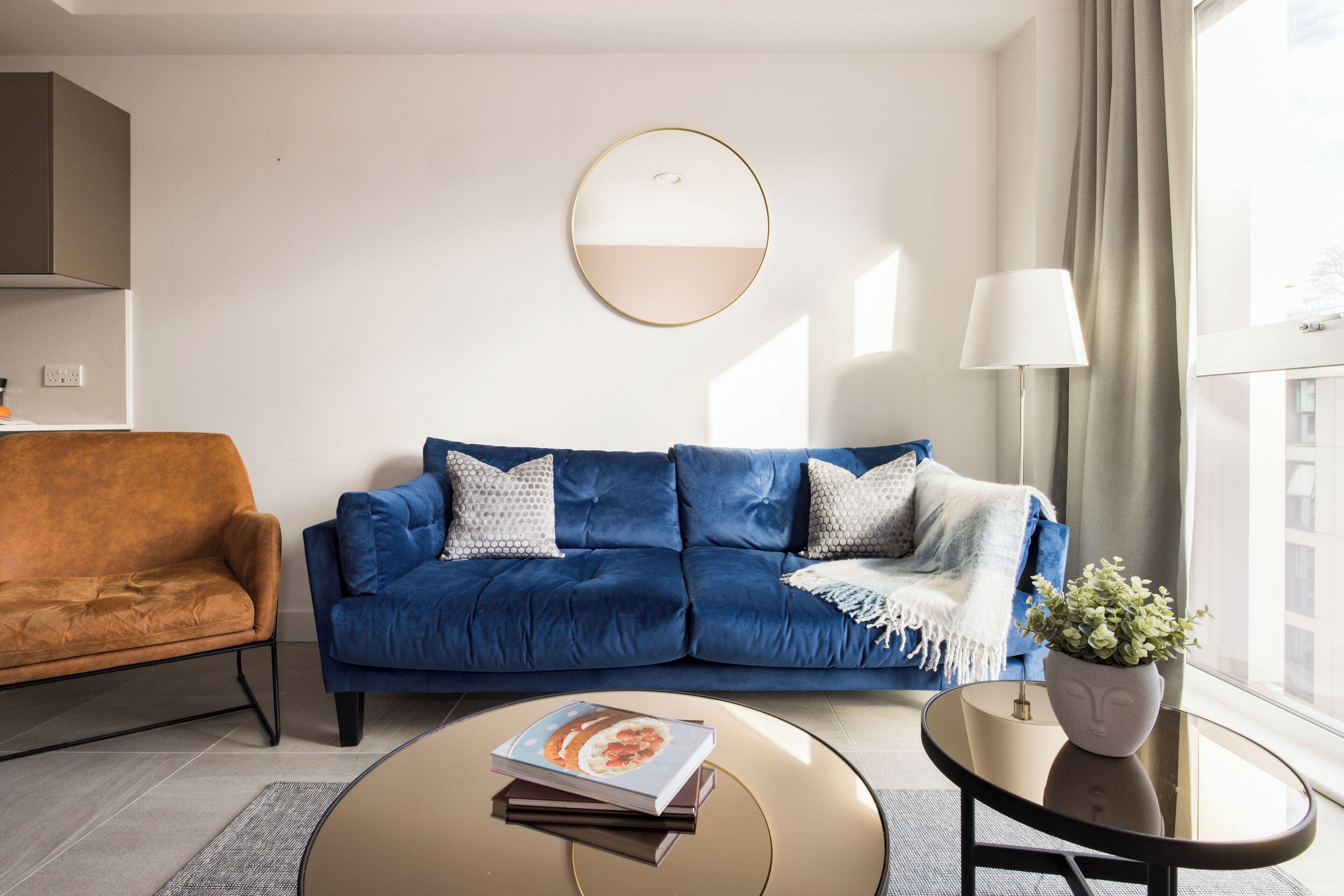 Un saló modern amb un sofà blau, un butàc armchair taronja, una taula de centre rodona i una planta en test.