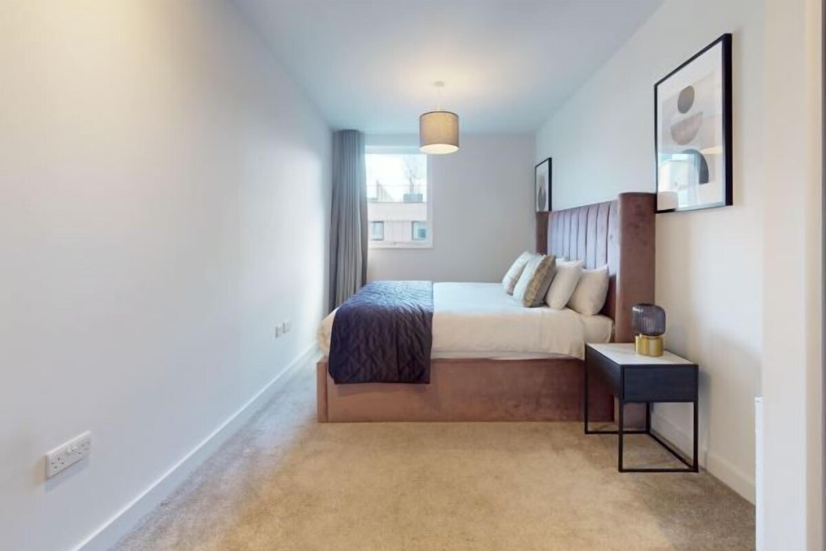 A bedroom with a bed, bedside table, lamp, and a window with curtains.