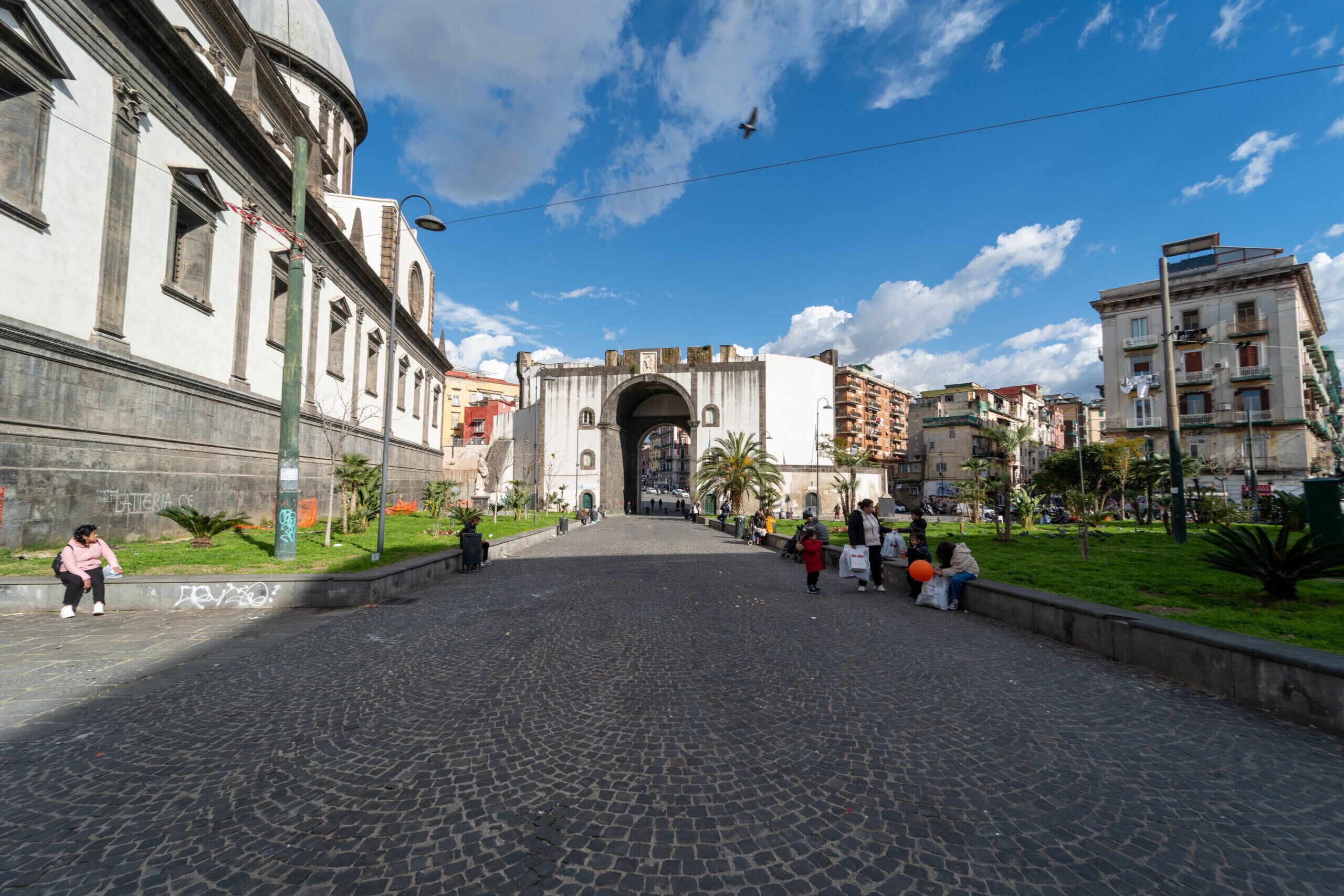 A cobblestone street leading to a historic archway with buildings on either side.