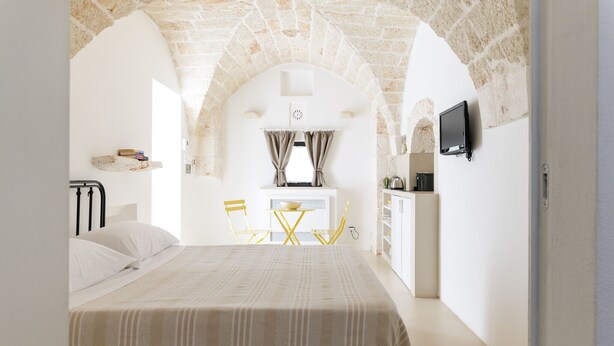 Une chambre avec un lit, une petite table, des chaises, un téléviseur et un coin cuisine.