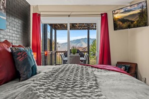 A bedroom with a bed, a view of mountains through an open door, and a TV on the wall. - Gatlinburg Family Chalet - Mountain Views - 3 Kings - Hot Tub + Sauna (Gatlinburg)