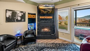 A living room with a fireplace, two leather chairs, a patterned rug, and a large window with a view of a deck.