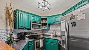 A kitchen with teal cabinets, a stainless steel refrigerator, a microwave, an oven, and a coffee maker.