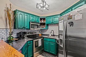 Una cocina con gabinetes color turquesa, un refrigerador de acero inoxidable, un microondas, un horno y una cafetera.