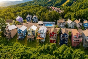 A residential area with houses on stilts, a swimming pool, and a forested backdrop.