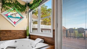A bathroom with a freestanding bathtub, a wooden vanity, a window with blinds, and a decorative stained glass window.