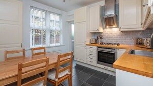 A modern kitchen with white cabinets, a wooden dining table, and a gas stove. - Ground Floor Apartment - Private Garden (London)