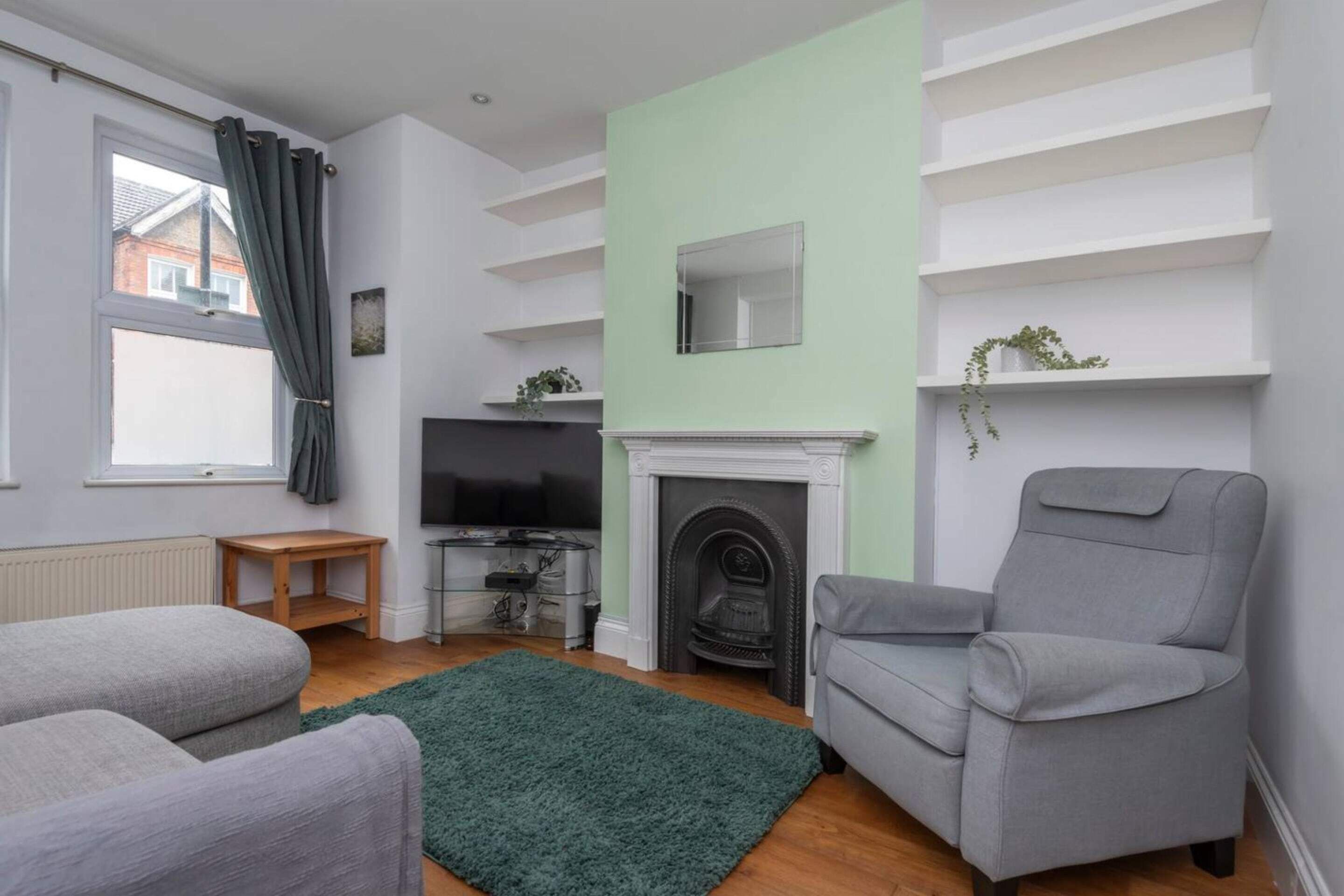 Un salon moderne avec une cheminée, des fauteuils gris, un tapis vert et un téléviseur.