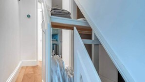 A narrow hallway with a wooden floor, a white door, and a white staircase with a built-in closet. - Ground Floor Apartment - Private Garden (London)