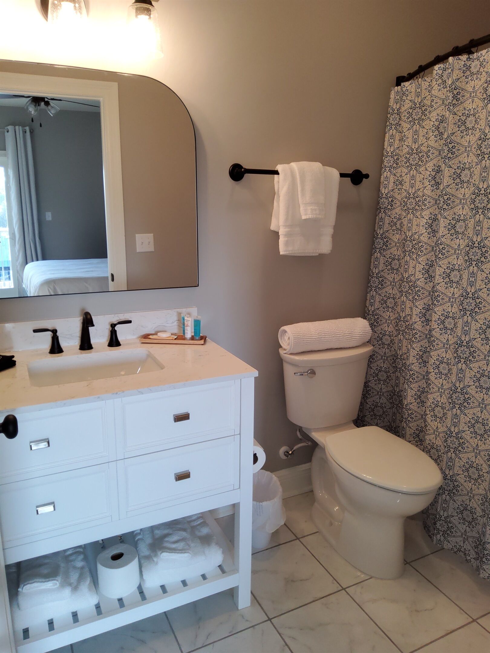 Une salle de bain avec un meuble-lavabo blanc, un miroir, des toilettes et un rideau de douche.