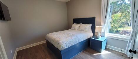 A bedroom with a bed, a nightstand, a ceiling fan, and a window with curtains.