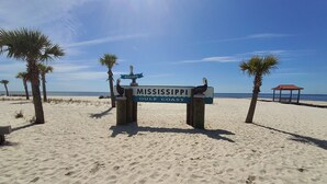 A beach sign with 'Mississippi Gulf Coast' written on it, surrounded by palm trees and a clear sky. - Four Palms Unit D, 500ft to Beach, Walk 2 Casinos! (Biloxi)