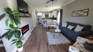 A modern living room with a fireplace, a ceiling fan, and a dining area in the background. - Four Palms Unit D, 500ft to Beach, Walk 2 Casinos! (Biloxi)