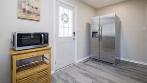 A kitchen with a stainless steel refrigerator, a microwave on a wooden cart, and a door with a wreath. - Pet friendly, huge fenced in yard, Fireplace, Firepit, near SGMC & VSU & Eats (Valdosta)