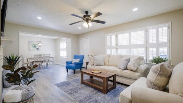 A spacious living room with a ceiling fan, a sofa, a coffee table, and a dining area with a table and chairs. - Pet friendly, huge fenced in yard, Fireplace, Firepit, near SGMC & VSU & Eats (Valdosta)